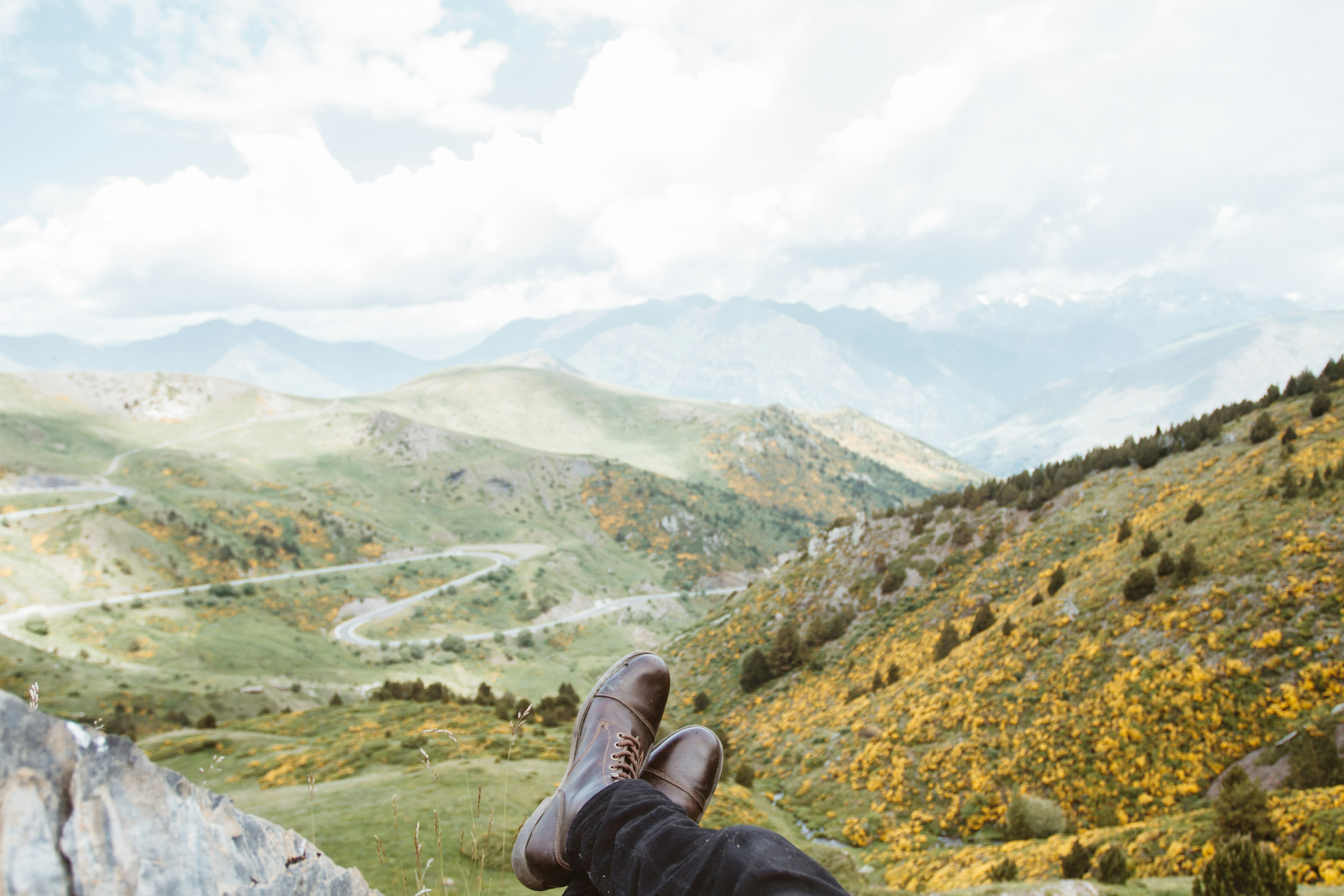 person wearing brown leather boots near mountains at daytime